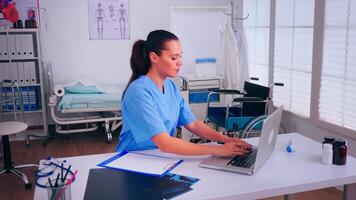 Healthcare assistant taking notes on clipboard and typing on laptop working in hospital clinic. Medical physician in medicine uniform writing list of consulted, diagnosed patients, making research. video