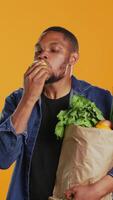 vertikal afrikansk amerikan vegan kille tar en bita från en mogen naturlig grön äpple, äter nyligen UPPTAGITS organisk frukt i studio. person reklam lokal- jordbruk och etiskt kommer från varor. kamera b. video