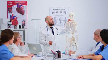 Medical doctor man pointing on cervical spine of human skeleton anatomical model, explaining to coworkers medical procedures in hospital meeting room. Physicians discussing about symptoms of disease video