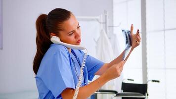 Medical nurse holding patient x-ray in hospital while talking with doctor on phone about man diagnosis. Healthcare physician in medicine uniform, doctor assistant helping with telehealth communication video