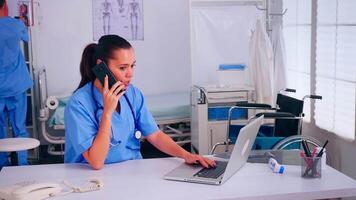 Nurse physician consulting remote patient using smartphone in hospital wearing medicine uniform. Doctor healthcare assistant helping patient with telehealth communication, diagnosing, typing on laptop video