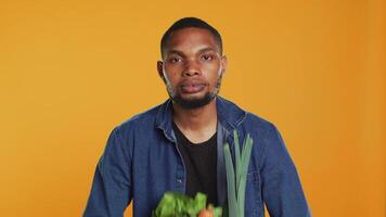 Young adult pretending to lift weight with a paper bag full of bio groceries, mimicking workout exercises in studio. Male model lifting a variety of ethically sourced fruits and veggies. Camera A. video