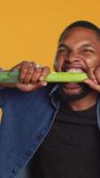 Vertical Young person biting on a green onion and acting silly in studio, pretending to eat a natural ethically sourced leek to advocate for sustainable lifestyle and veganism. Camera A. video