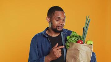 African american person pointing at ethically sourced fruits and veggies stored in a paper bag, making eco friendly recommendations for healthy eating and vegan nutrition. Camera A. video