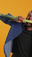 Vertical Young person biting on a green onion and acting silly in studio, pretending to eat a natural ethically sourced leek to advocate for sustainable lifestyle and veganism. Camera B. video