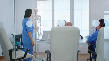 Medical nurse pointing on cervical spine of human skeleton anatomical model, explaining to coworkers medical procedures in hospital meeting room. Physicians discussing about symptoms of disease video