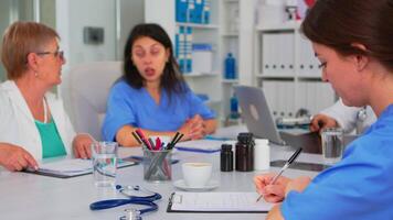 Krankenschwester Schreiben auf Zwischenablage während professionell Teamarbeiter haben medizinisch Treffen diskutieren im Hintergrund im Brainstorming Büro. professionell Ärzte Prüfung das Symptome von geduldig im Treffen Zimmer. video