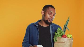 Relaxed carefree person drinking a coffee cup and carrying his groceries, going shopping at a local farmers market. Male model enjoying refreshment against orange background. Camera A. video