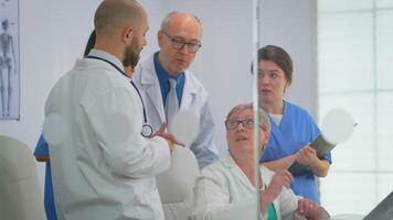 team van artsen staand in conferentie ziekenhuis kamer, senior dokter bespreken over behandeling voor geduldig op zoek in laptop. collega's in wit jassen werken samen analyseren symptomen van ziekte video