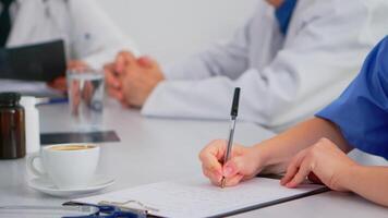 Close up of nurse writing on clipboard while coworkers discussing in background analysing patients radiography. Profesional teamworkers having medical meeting, brainstorming in hospital office. video