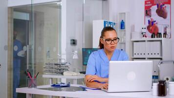 müde medizinisch Assistent mit Kopfschmerzen nehmen aus das Brille und entspannend nach Arbeiten beim Laptop im Krankenhaus Klinik. erschöpft Therapeut im Medizin Uniform nehmen brechen ruhen Augen video