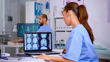 Doctor assistant analyzing skull brain x-ray tommography medical data on laptop, taking notes on clipboard. Radiologist in medicine uniform looking at digital radiography, examination, diagnosis. video