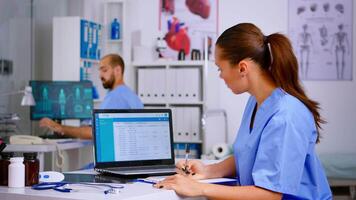 médico médico enfermeira segurando e analisando radiografia verificação tratamento do diagnosticado pacientes, escrevendo informações dentro computador portátil. assistente trabalhando dentro hospital fazer compromissos e cadastro. video