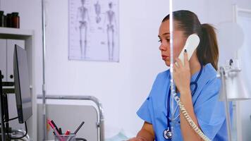 specialist sjukvård läkare talande på telefon i medicin klinik, receptionist läkare assistent portion med telehälsa konkulation. sjuksköterska arbetssätt i sjukhus kontroll registrering på dator video