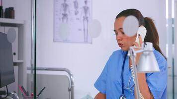 Medical assistant talking at phone and typing on computer offering consultation in hospital clinic. Woman receptionist in medicine uniform, doctor nurse assistant helping with telehealth communication video
