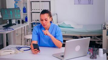 Professional woman assistant giving online medical consultation using smartphone from private modern clinic. Remote healthcare service, health conference, telemedicine, virtual meeting video