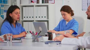 Woman assistent typing on laptop at desk looking at camera and smiling in busy workday in modern medical office. Woman specialist writing on notepad during brainstorming in meeting room video