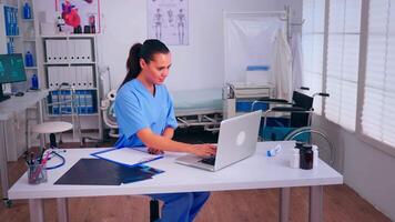 terapeuta escritura lista de consultado pacientes en línea, haciendo investigación, tomando nota, tomando útil información en portapapeles. médico asistente en uniforme trabajando en ordenador portátil en moderno hospital oficina. video