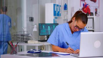 Exhausted therapist working on laptop and taking off the glasses having headache in hospital. Distraught therapist student practicing medicine writing on clipboard list of diagnosed patients video