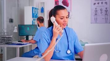 médico equipe trabalhando dentro hospital, enfermeira falando em telefone e colega digitando em pc. cuidados de saúde médico dentro uniforme, médico enfermeira assistente ajudando com telessaúde comunicação, controlo remoto consulta video