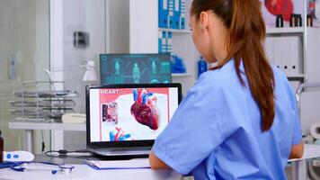 assistente perícia médico dentro médico uniforme examinando coração doença usando computador portátil, escrevendo em prancheta informações. médico enfermeira analisando remédio documentos, diagnóstico do pacientes, equipe de trabalho video