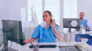 mujer recepcionista respondiendo a teléfono, trabajando en hospital clínica escritura en computadora, haciendo equipo. médico médico en uniforme escritura lista de consultado, diagnosticado pacientes, haciendo investigación. video