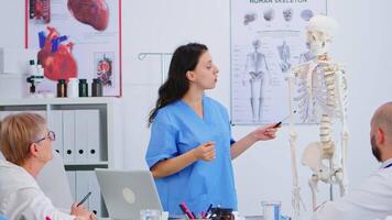 médico describiendo el diseño de el humano espina en frente de colegas utilizando esqueleto modelo explicando médico procedimientos en pie en hospital oficina. medicos que se discute acerca de síntomas de enfermedad video