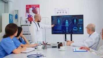Man doctor presenting human internal structure in front of attantive colleagues using digital monitor in hospital meeting office during brainstorming. Medical team analysing diagnosis of patients video