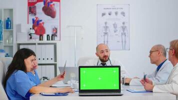 médico colegas trabalhando dentro hospital conferência quarto analisando pacientes relatórios colocação computador portátil com verde tela dentro frente do Câmera. usando computador com zombar acima exibição verde croma chave dentro clínica. video