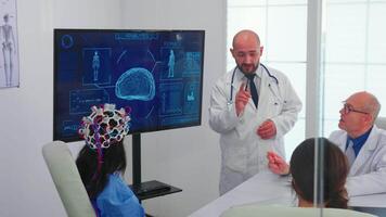 läkare talande handla om hjärna aktivitet under konferens med medicinsk personal och sjuksköterska bär headsetet med sensorer. övervaka visar modern hjärna studie medan team av forskare justerar de enhet. video