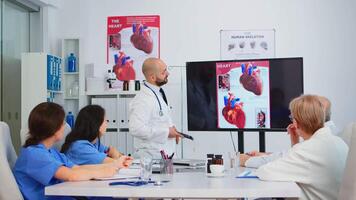 erfaren man läkare analyserar hjärta frågor bild tillsammans med kvalifierad kollegor i möte rum, pekande på övervaka. doktorer diskuterar diagnos handla om behandling av patienter video