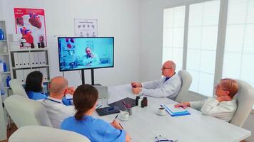 Mannschaft von medizinisch Mitarbeiter diskutieren während Konferenz mit Arzt im Krankenhaus Büro. Ärzte halten online Treffen im Sitzungssaal mit Mann Spezialist, Krankenschwester nehmen Anmerkungen auf Zwischenablage. video