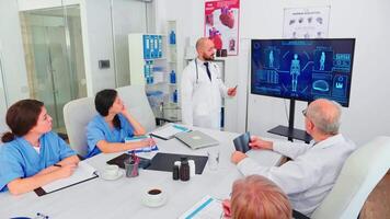 Medical expert talking about healthcare during seminar with hospital staff in conference room pointing at digital monitor. Clinic herapist discussing with colleagues about disease, medicine professional video