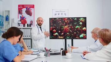 specialist läkare förklara virus utveckling på digital skärm i främre av medarbetare pekande på övervaka i sjukhus kontor under brainstorming. team av physicians analyserar diagnos av patienter video