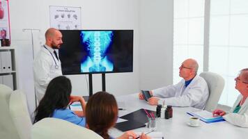 gruppo di medici ascoltando medico esperto durante medico conferenza analizzando digitale radiografia, puntamento su tenere sotto controllo. medici utilizzando moderno tecnologia discutere diagnosi di pazienti trattamento video