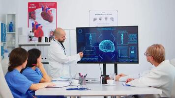 Medical worker presenting report on digital screen about internal human brain in front of colleagues pointing on monitor in hospital office during brainstorming. Team analysing diagnosis of patients video