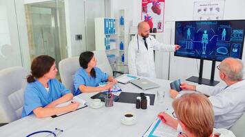 Mature medical physician explaining treatment to nurses during healthcare seminar pointing at digital monitor. Clinic herapist discussing with colleagues about disease, medicine professional. video