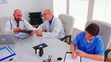 artsen hebben een medisch discussie over radiografie gedurende team vergadering terwijl verpleegster nemen notities. kliniek deskundige therapeut pratend met collega's over ziekte, geneeskunde professioneel. video