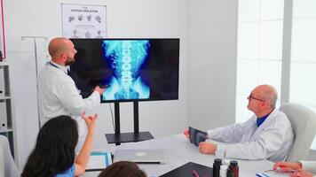 Expert doctor holding medical training using modern technology, presenting digital radiography to coworkers. Radiologist analysing x-ray spin image discussing symptoms of disease for further treatment video