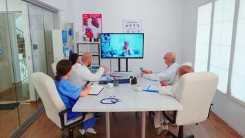 grupp av doktorer diskuterar med expert- läkare under konferens från sjukhus kontor. medicin personal använder sig av internet under uppkopplad möte med expert- läkare för expertis, sjuksköterska tar anteckningar. video
