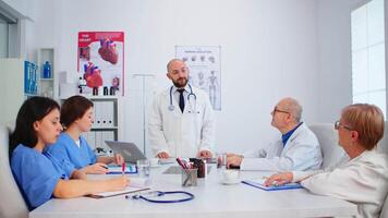 Medical team listening specialist doctor and taking notes during brainstorming sitting in hospital meeting room. Surgeon explaining treatment to coworkers presenting plan during medical conference video