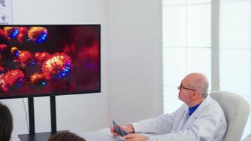 läkare innehav presentation handla om coronavirus under möte med medicinsk personal använder sig av digital övervaka. virologist analyserar med kollegor farlig virus, symptom arbetssätt i sjukhus kontor video