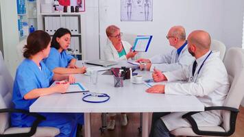 médico mujer practicante escritura notas en portapapeles vistiendo azul uniforme durante conferencia con compañeros de trabajo clínica experto terapeuta hablando con colegas acerca de enfermedad, medicina profesional. video