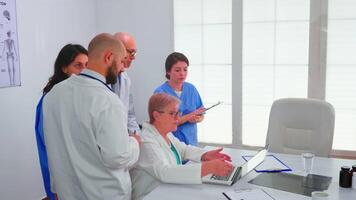 médico equipo teniendo un discusión acerca de paciente diagnóstico mirando a ordenador portátil pantalla en conferencia habitación. clínica experto terapeuta que se discute diagnóstico acerca de pacientes tratamiento cuestiones grabar en lugar de trabajo. video