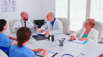 doctores analizando lista de paciente hablando con colegas acerca de síntomas y tratamiento. médico equipo teniendo conferencia que se discute acerca de pacientes enfermedad sentado en hospital oficina video