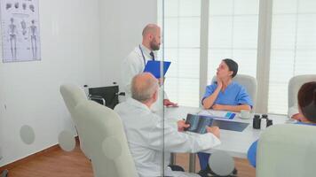 Medical practitioner presenting diagnosis to colleagues holding clipboard during briefing with coworkers. Clinic expert therapist talking with colleagues about disease, medicine professional video