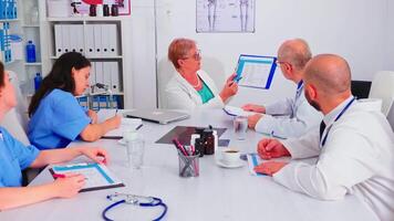 médico enfermero escritura en portapapeles durante cuidado de la salud seminario en hospital reunión oficina acerca de clientela lista. clínica experto terapeuta hablando con colegas acerca de enfermedad, medicina profesional. video