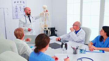 expert- radiolog demonstrera på skelett under genomgång med medicinsk personal i sjukhus möte rum. klinik terapeut talande med kollegor handla om sjukdom, medicin professionell video
