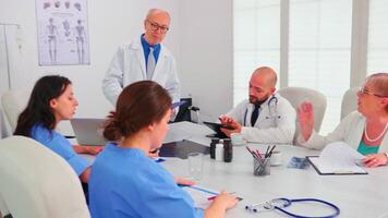 Female nurse taking notes while elderly medical expert explaining viral diseases in hospital conference room. Clinic expert therapist talking with colleagues about disease, medicine professional video