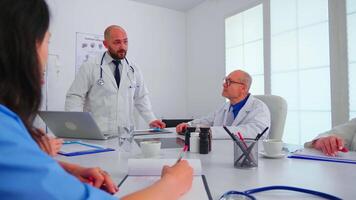 Medical staff talking with teamworker practitioner wearing white coat in hospital meeting room. Clinic therapist with colleagues talking about disease, expert,specialist, communication. video